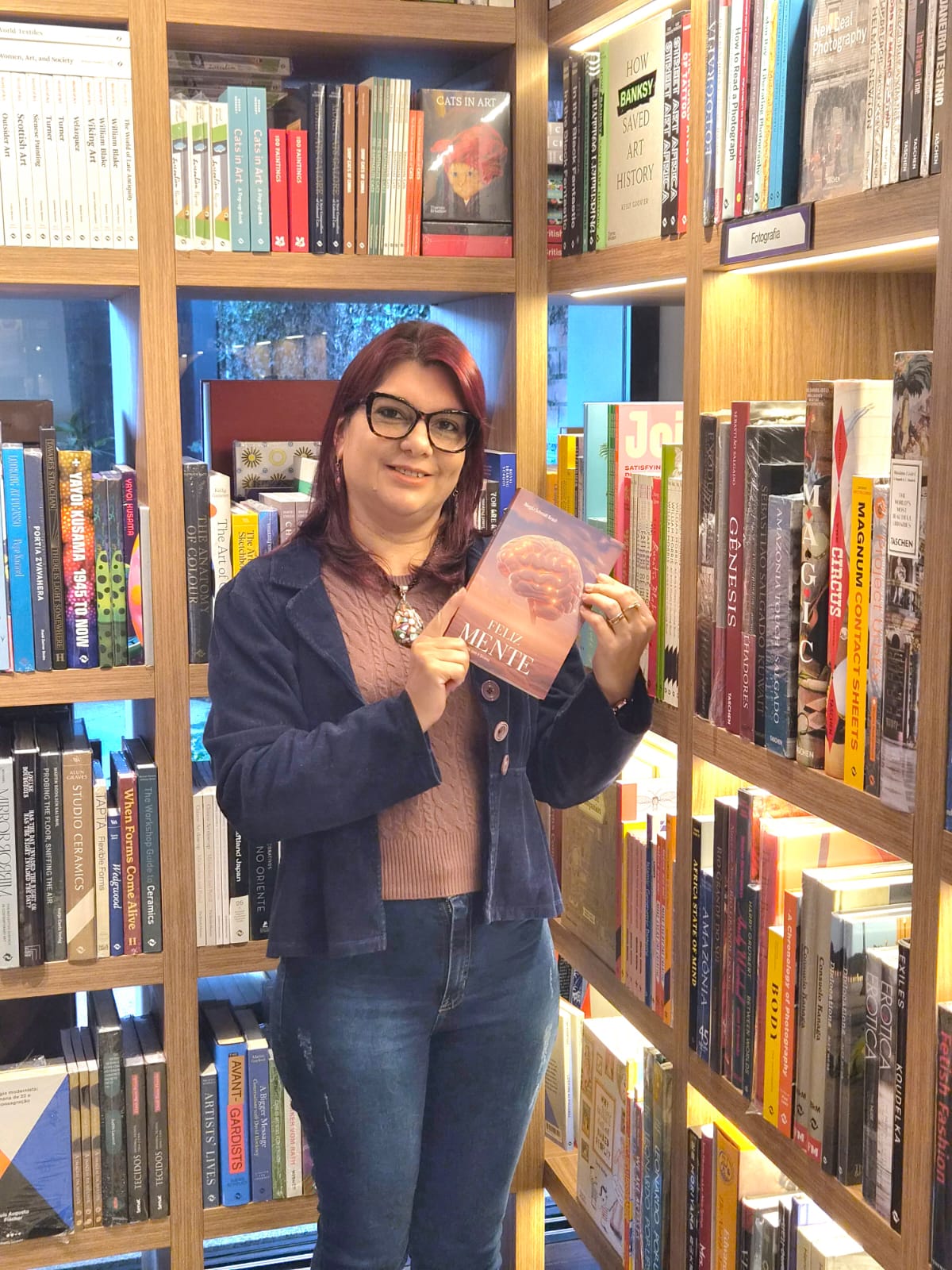 Magda segurando o livro FelizMENTE em uma livraria